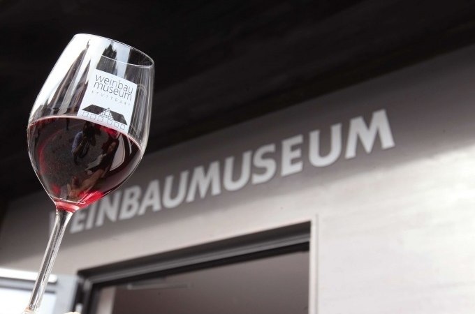 Ein Weinglas mit Rotwein wird vor dem Eingang des Weinbaumuseums in die Höhe gehalten., © Stuttgart Marketing GmbH, Thomas NIedermüller Ein Weinglas mit Rotwein wird vor dem Eingang des Weinbaumuseums in die Höhe gehalten., © Stuttgart Marketing GmbH, Thomas NIedermüller