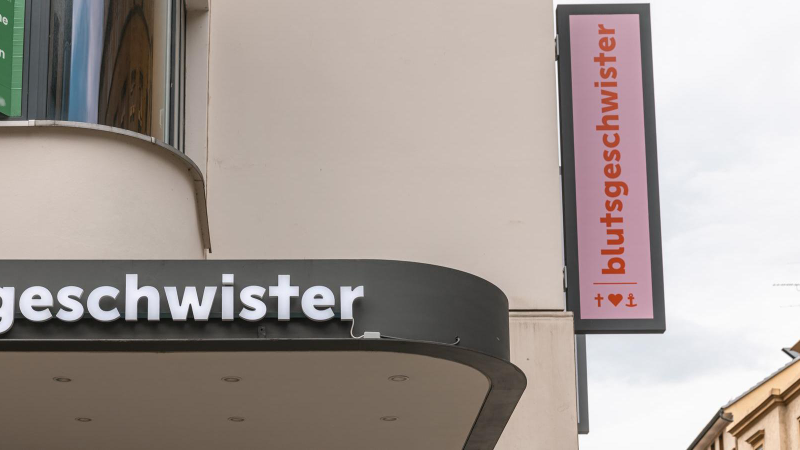 Ein Geschäftsschild mit der Aufschrift 'blutsgeschwister' an einem Gebäude. Ein weiteres Schild zeigt das Logo mit Herz und Anker., © Stuttgart-Marketing GmbH, Sarah Schmid