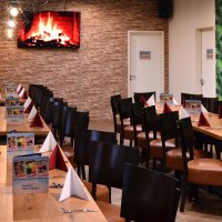 Ein langer Tisch in einer Lounge, dekoriert mit roten und weißen Servietten. An der Wand ein Bildschirm mit Kaminfeuer, daneben eine grüne Tapete., © Bowling & Billard Lounge