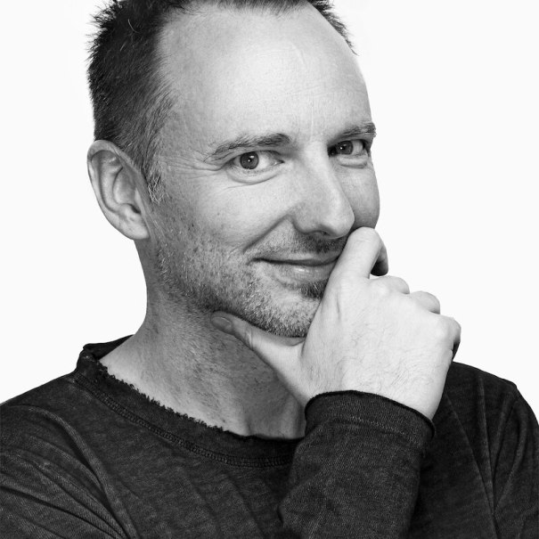 Schwarz-weiß Porträt eines Mannes, der lächelnd in die Kamera schaut und seine Hand nachdenklich ans Kinn legt., © Mauerwerk GmbH