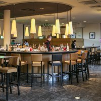 Moderne Bar mit runder Theke, Hängelampen und Sitzbereichen im Arcotel Camino. Menschen sitzen und genießen die Atmosphäre., © Harald Eisenberger