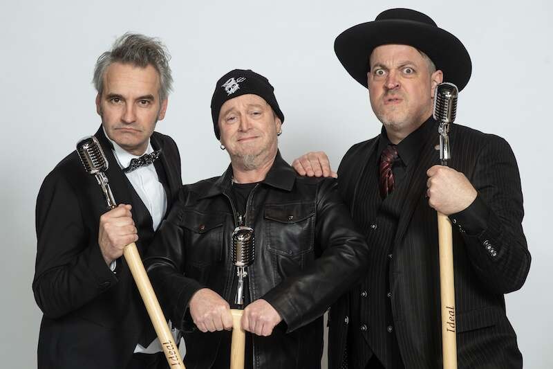 Drei Männer posieren mit Mikrofonen. Einer trägt eine Fliege, der andere einen Hut, der dritte eine Mütze. Sie wirken humorvoll und selbstbewusst., © C² CONCERTS GmbH