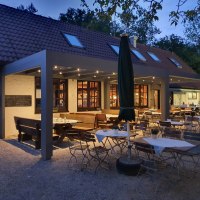 Gemütlicher Außenbereich eines Restaurants bei Dämmerung, mit Holztischen und -stühlen unter einem überdachten Bereich. Beleuchtung sorgt für eine warme Atmosphäre., © Kräuterbühl Gemütlicher Außenbereich eines Restaurants bei Dämmerung, mit Holztischen und -stühlen unter einem überdachten Bereich. Beleuchtung sorgt für eine warme Atmosphäre., © Kräuterbühl