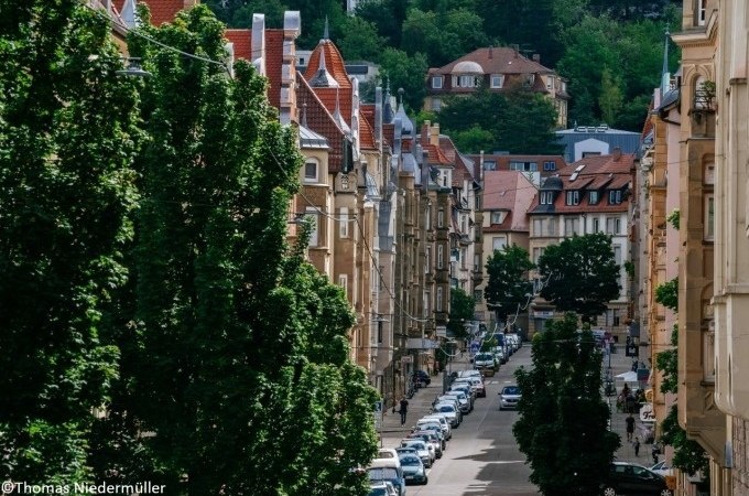 Straße in Stuttgart mit historischen Gebäuden, Bäumen und parkenden Autos. Im Hintergrund sind grüne Hügel und weitere Häuser zu sehen., © Stuttgart Marketing GmbH