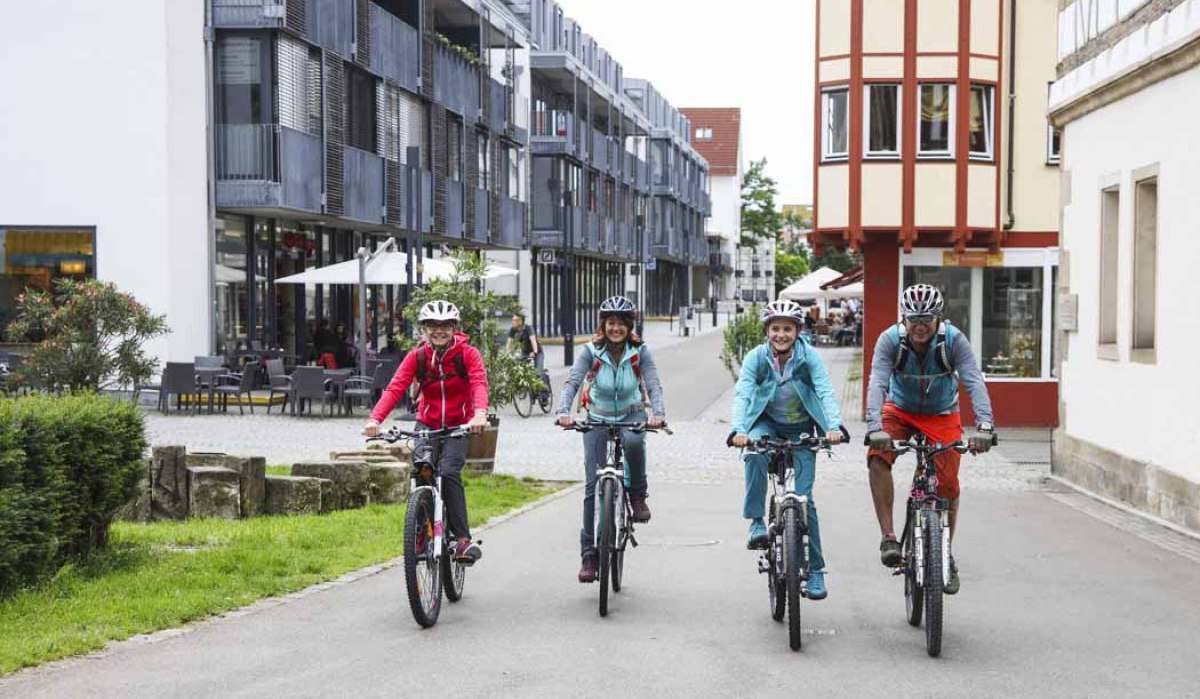 Vier Personen fahren mit Fahrrädern durch eine moderne Straße in Kirchheim unter Teck. Sie tragen Helme und Freizeitkleidung., © Schwäbische Alb Tourismusverband e.V. Vier Personen fahren mit Fahrrädern durch eine moderne Straße in Kirchheim unter Teck. Sie tragen Helme und Freizeitkleidung., © Schwäbische Alb Tourismusverband e.V.