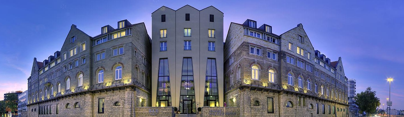 Das Arcotel Camino bei Dämmerung, mit beleuchteten Fenstern und einem klaren Himmel im Hintergrund. Historische Fassade mit modernen Elementen., © www.fnoxx.de