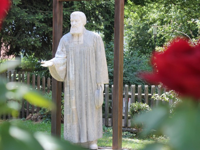 Statue von Johannes Brenz in einem Garten, umgeben von B&auml;umen und Blumen im Vordergrund. Ein Holzzaun ist im Hintergrund sichtbar., &copy; Stadtverwaltung Weil der Stadt