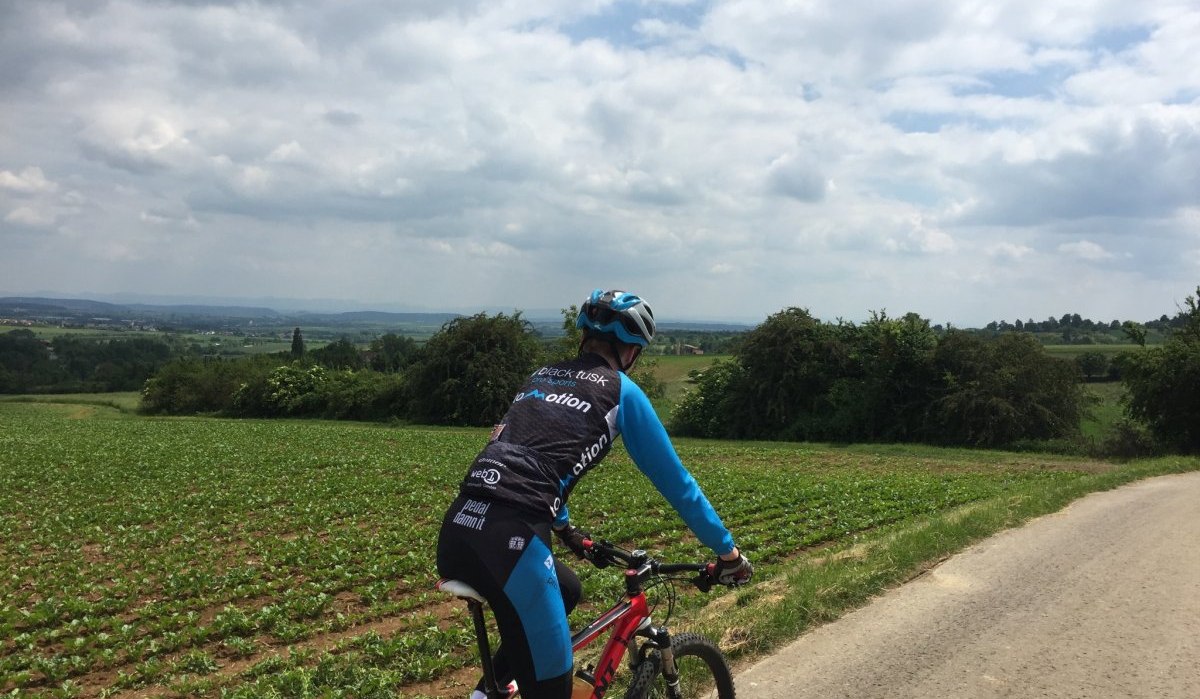 Ein Radfahrer auf einem Feldweg schaut &uuml;ber eine weite, gr&uuml;ne Landschaft. Der Himmel ist bew&ouml;lkt, und die Umgebung wirkt ruhig und l&auml;ndlich., &copy; Natur.Nah. Sch&ouml;nbuch & Heckeng&auml;u