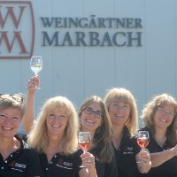 Sieben Personen heben lächelnd Weingläser vor einem Gebäude mit 'Weingärtner Marbach'-Logo., © Weingärtner Marbach e. G. Sieben Personen heben lächelnd Weingläser vor einem Gebäude mit 'Weingärtner Marbach'-Logo., © Weingärtner Marbach e. G.