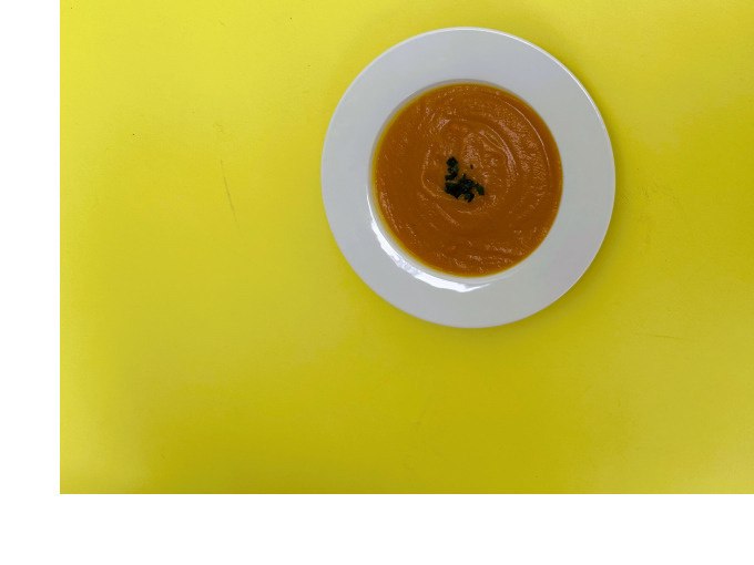 Ein weißer Teller mit orangefarbener Suppe, garniert mit Kräutern, auf einem leuchtend gelben Hintergrund., © Kunsthalle Göppingen Ein weißer Teller mit orangefarbener Suppe, garniert mit Kräutern, auf einem leuchtend gelben Hintergrund., © Kunsthalle Göppingen