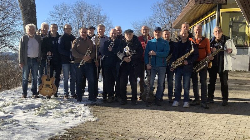 Die Herrenberg Bigband posiert mit Instrumenten im Freien vor einem Geb&auml;ude. Der Boden ist teils schneebedeckt, die Sonne scheint und B&auml;ume sind im Hintergrund sichtbar., &copy; Interessengemeinschaft Kultur Sindelfingen / B&ouml;blingen e.V.