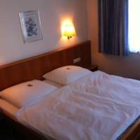 Ein gemütliches Doppelzimmer mit einem großen Bett, zwei Wandlampen und einem Bild an der Wand. Ein Fenster mit Vorhängen ist zu sehen., © Hotel Sonne garni Ein gemütliches Doppelzimmer mit einem großen Bett, zwei Wandlampen und einem Bild an der Wand. Ein Fenster mit Vorhängen ist zu sehen., © Hotel Sonne garni