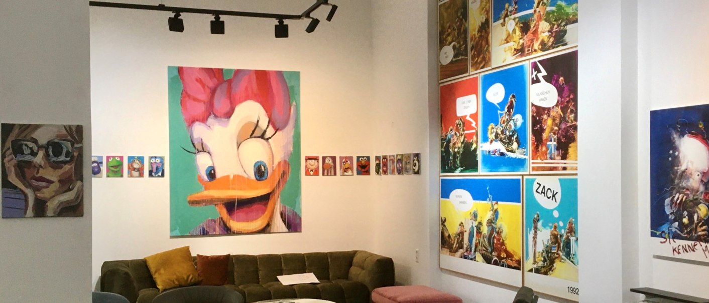 Eine Galerie zeigt bunte Pop-Art-Gem&auml;lde von Comicfiguren und moderne Kunstwerke. Ein gro&szlig;es Bild einer Ente dominiert die Wand. Ein Sofa steht im Raum., &copy; GALERIE Z