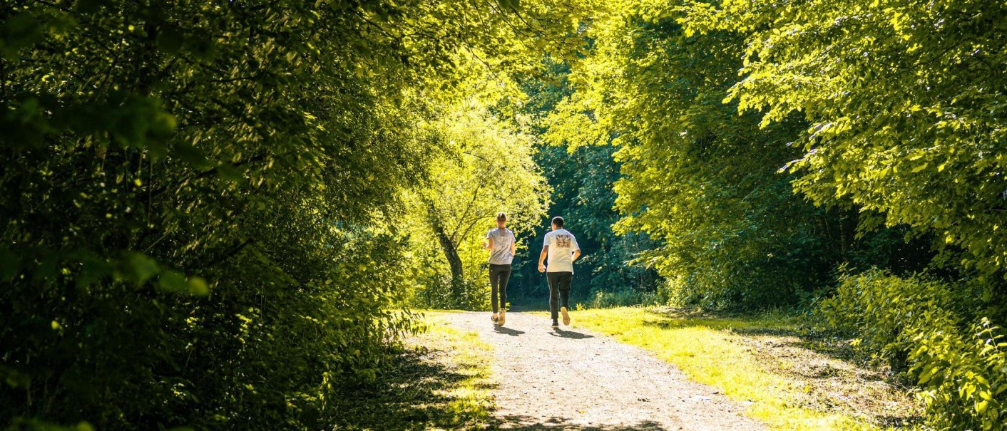 Zwei Personen spazieren auf einem sonnigen Waldweg, umgeben von üppigem Grün. Die Szene strahlt Ruhe und Naturverbundenheit aus., © Stuttgart-Marketing GmbH, Sarah Schmid Zwei Personen spazieren auf einem sonnigen Waldweg, umgeben von üppigem Grün. Die Szene strahlt Ruhe und Naturverbundenheit aus., © Stuttgart-Marketing GmbH, Sarah Schmid