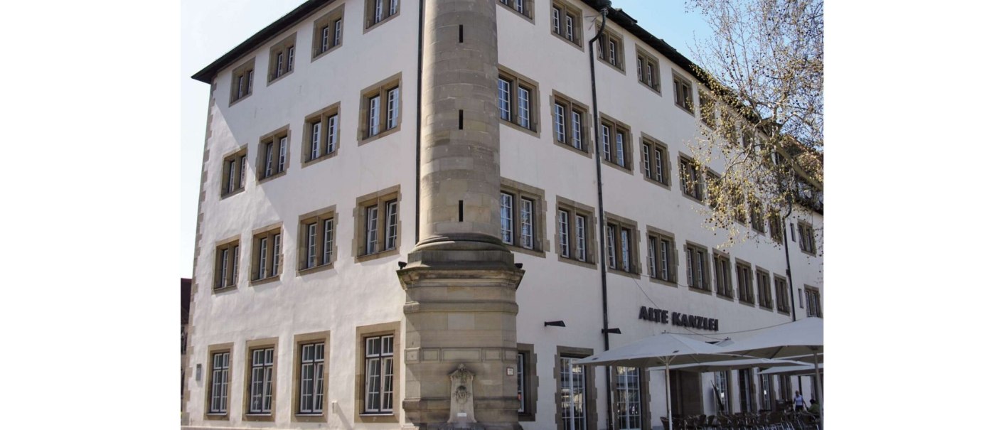 Die Alte Kanzlei in Stuttgart, ein historisches Gebäude mit vielen Fenstern, einem markanten Eckpfeiler und einem Außenbereich mit Sonnenschirmen., © Stuttgart-Marketing GmbH