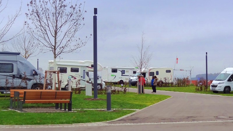 Wohnmobilstellplatz mit mehreren Wohnmobilen, kahlen B&auml;umen und einer Bank. Zwei Personen stehen auf dem Weg. Tr&uuml;bes Wetter., &copy; Panorama Therme Beuren, Birgit Eschment