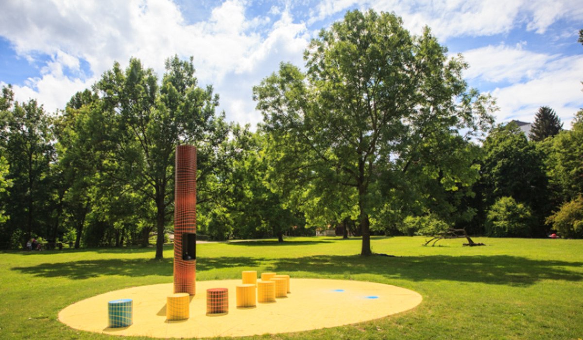 Kunstinstallation im Freien mit bunten Säulen auf gelbem Boden, umgeben von grünen Bäumen und blauem Himmel., © Kai Köpf