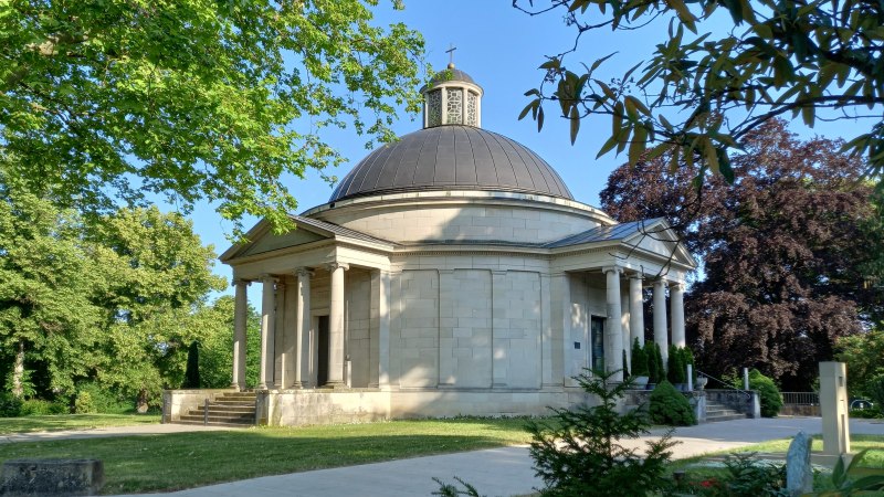 Frasch Mausoleum auf dem Friedhof in Gaildorf: helles Steingeb&auml;ude mit grauer Kuppel umgeben von B&auml;umen und Gr&uuml;nfl&auml;chen. Von S&auml;ulen getragene Vord&auml;cher sch&uuml;tzen zwei Eingangst&uuml;ren, zu denen Stufen hinauff&uuml;hren., &copy; Petra Natzkowski