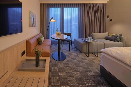 Modernes Hotelzimmer mit Sofa, Tisch, Bett und großen Fenstern. Dezente Beleuchtung und stilvolle Dekoration schaffen eine gemütliche Atmosphäre., © Adina Apartment Hotel Stuttgart Modernes Hotelzimmer mit Sofa, Tisch, Bett und großen Fenstern. Dezente Beleuchtung und stilvolle Dekoration schaffen eine gemütliche Atmosphäre., © Adina Apartment Hotel Stuttgart