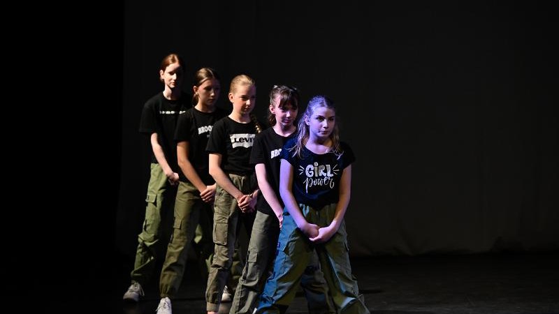 F&uuml;nf Kinder in schwarzen T-Shirts und gr&uuml;nen Hosen tanzen auf einer B&uuml;hne. Sie stehen in einer Reihe und tragen wei&szlig;e Turnschuhe., &copy; Kunstschule Labyrinth