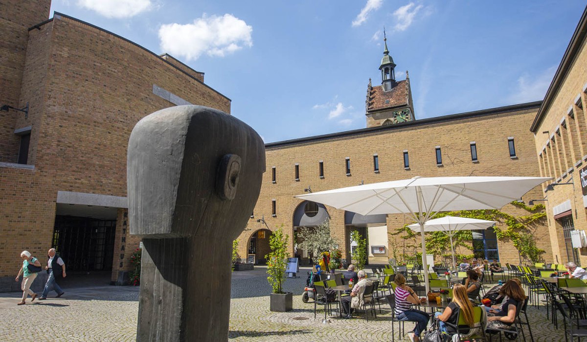 Ein Innenhof mit einer Holzskulptur im Vordergrund, Sitzbereich mit Sonnenschirmen und der Turm der Lutherkirche im Hintergrund., © Achim Mende Ein Innenhof mit einer Holzskulptur im Vordergrund, Sitzbereich mit Sonnenschirmen und der Turm der Lutherkirche im Hintergrund., © Achim Mende