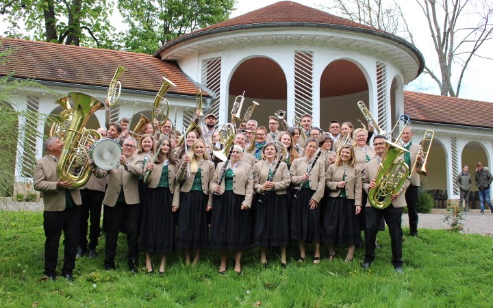 Eine Blaskapelle in traditioneller Kleidung steht vor einem runden Gebäude mit Bögen und rotem Dach., © Musikverein Bad Boll Eine Blaskapelle in traditioneller Kleidung steht vor einem runden Gebäude mit Bögen und rotem Dach., © Musikverein Bad Boll