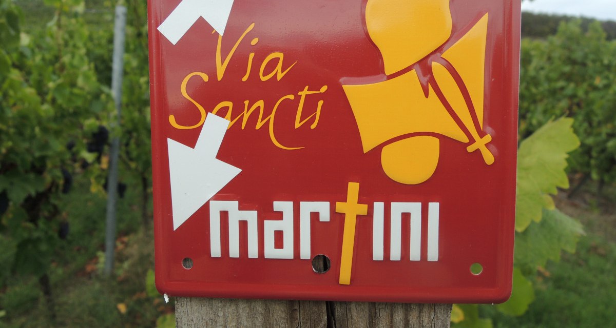 Rotes Schild mit 'Via Sancti Martini' und Pfeilen, befestigt an einem Holzpfosten in einem Weinberg., © Land der 1000 Hügel - Kraichgau-Stromberg Rotes Schild mit 'Via Sancti Martini' und Pfeilen, befestigt an einem Holzpfosten in einem Weinberg., © Land der 1000 Hügel - Kraichgau-Stromberg