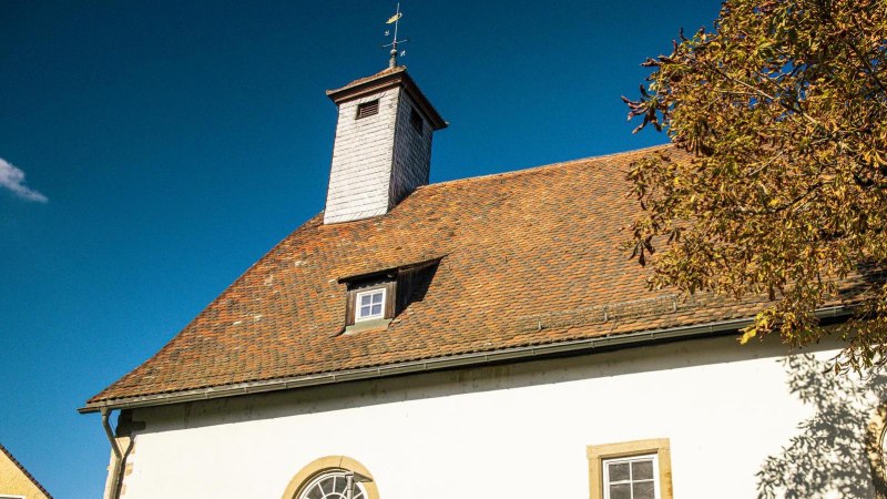 Die Peterskirche in Vaihingen an der Enz mit rotem Ziegeldach, kleinem Turm und einem Baum mit Herbstlaub vor blauem Himmel., © Stuttgart-Marketing GmbH, Sarah Schmid