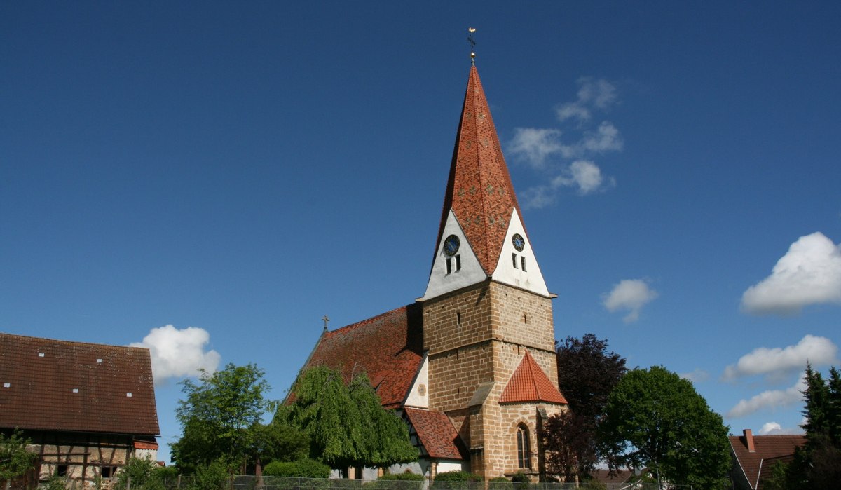 Die Johanneskirche in Gingen steht unter einem klaren blauen Himmel mit vereinzelten Wolken. Umgeben von Bäumen und traditionellen Gebäuden., © Landkreis Göppingen Die Johanneskirche in Gingen steht unter einem klaren blauen Himmel mit vereinzelten Wolken. Umgeben von Bäumen und traditionellen Gebäuden., © Landkreis Göppingen