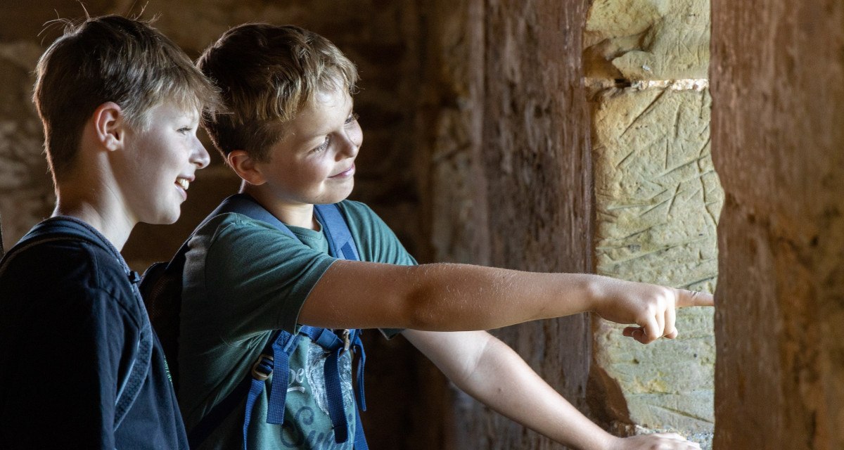 Zwei Jungen stehen in einer Burgruine und schauen lächelnd aus einem Fenster. Einer zeigt nach draußen., © Foto Thomas Zehnder Zwei Jungen stehen in einer Burgruine und schauen lächelnd aus einem Fenster. Einer zeigt nach draußen., © Foto Thomas Zehnder