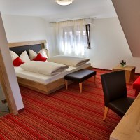 Ein gemütliches Hotelzimmer mit Doppelbett, rotem Sofa, Schreibtisch und Bad. Rote Akzente und Holzmöbel schaffen eine einladende Atmosphäre., © Hotel & Gasthof Ochsen