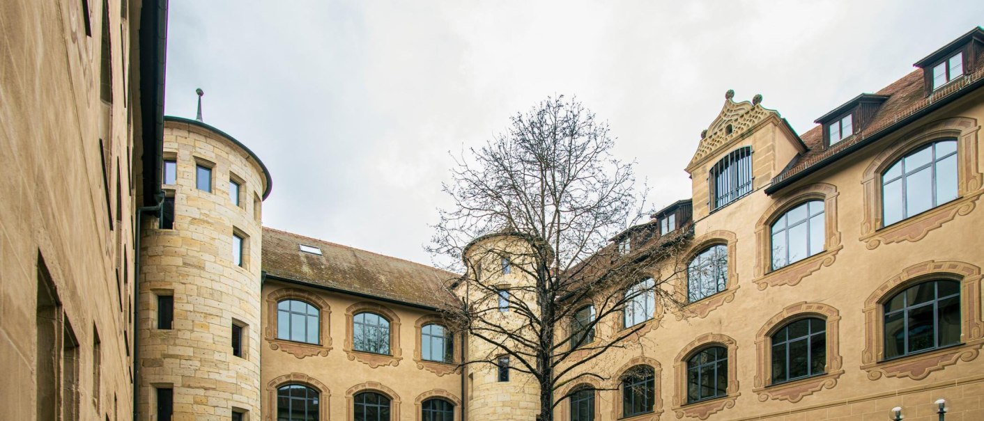 Innenhof eines historischen Geb&auml;udes mit Rundturm, gro&szlig;en Fenstern und einem kahlen Baum in der Mitte. Der Himmel ist bew&ouml;lkt., &copy; Stuttgart-Marketing GmbH, Sarah Schmid