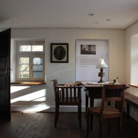 Historisches Zimmer im Christian-Wagner-Haus mit Holztisch, Stühlen, Lampe und Fenster. Bilder und Texte an den Wänden., © Stadt Leonberg