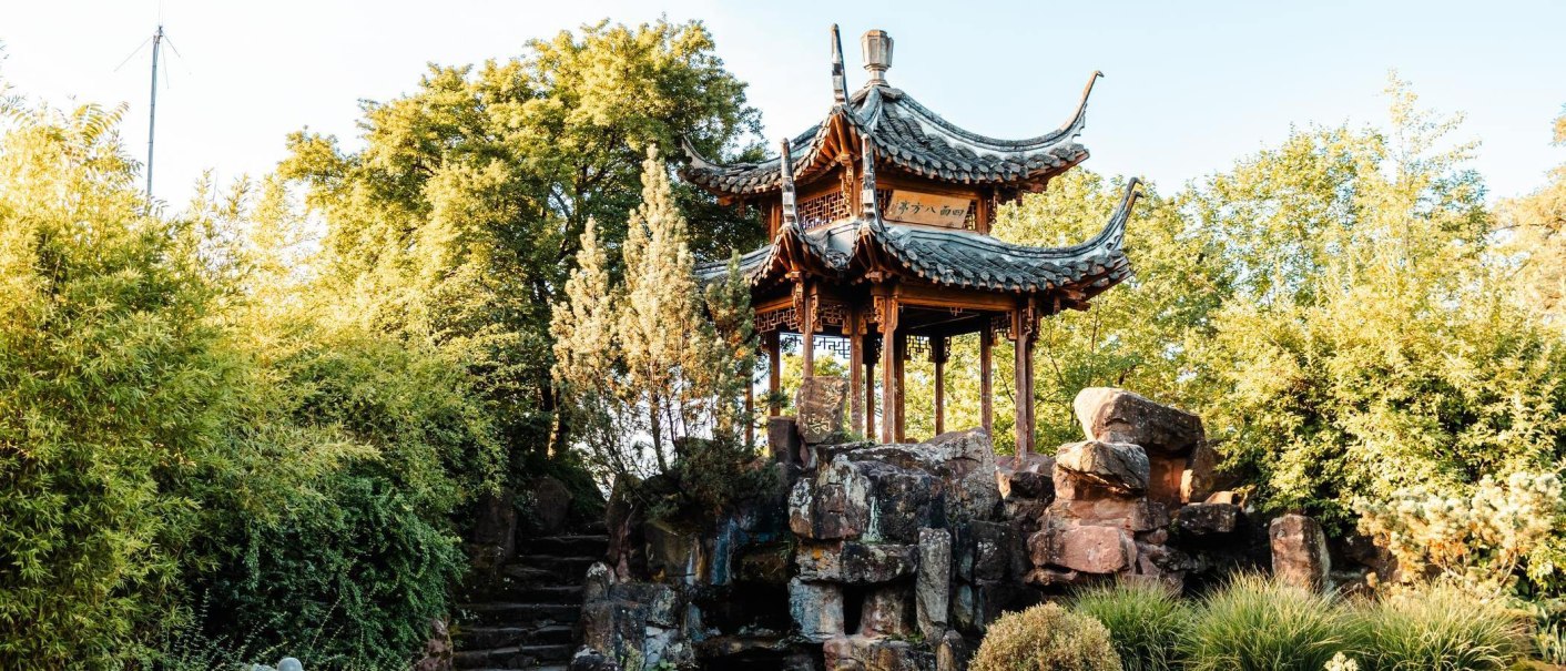 Ein traditioneller chinesischer Pavillon steht auf einem Felsen, umgeben von üppigem Grün im Chinesischen Garten Stuttgart., © Stuttgart-Marketing GmbH, Sarah Schmid