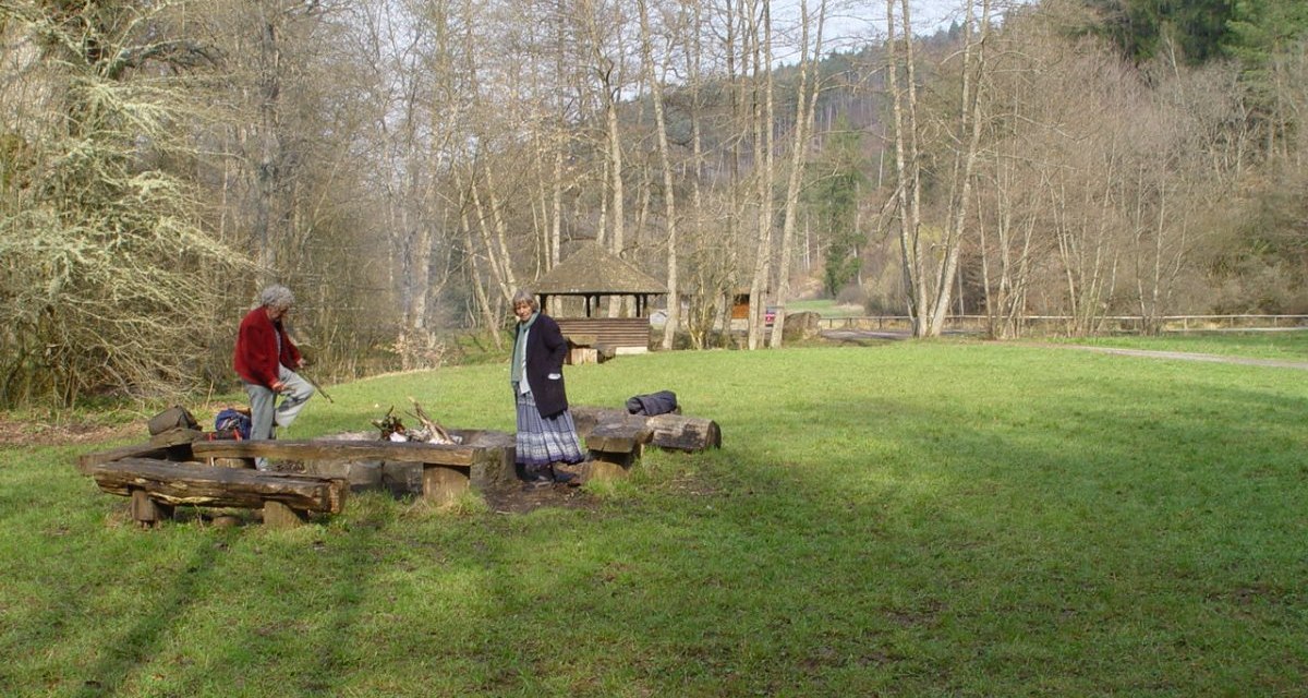 Zwei Personen stehen an einer Feuerstelle auf einer Wiese, umgeben von kahlen Bäumen. Im Hintergrund ist eine Holzhütte zu sehen., © Naturpark Schönbuch Zwei Personen stehen an einer Feuerstelle auf einer Wiese, umgeben von kahlen Bäumen. Im Hintergrund ist eine Holzhütte zu sehen., © Naturpark Schönbuch