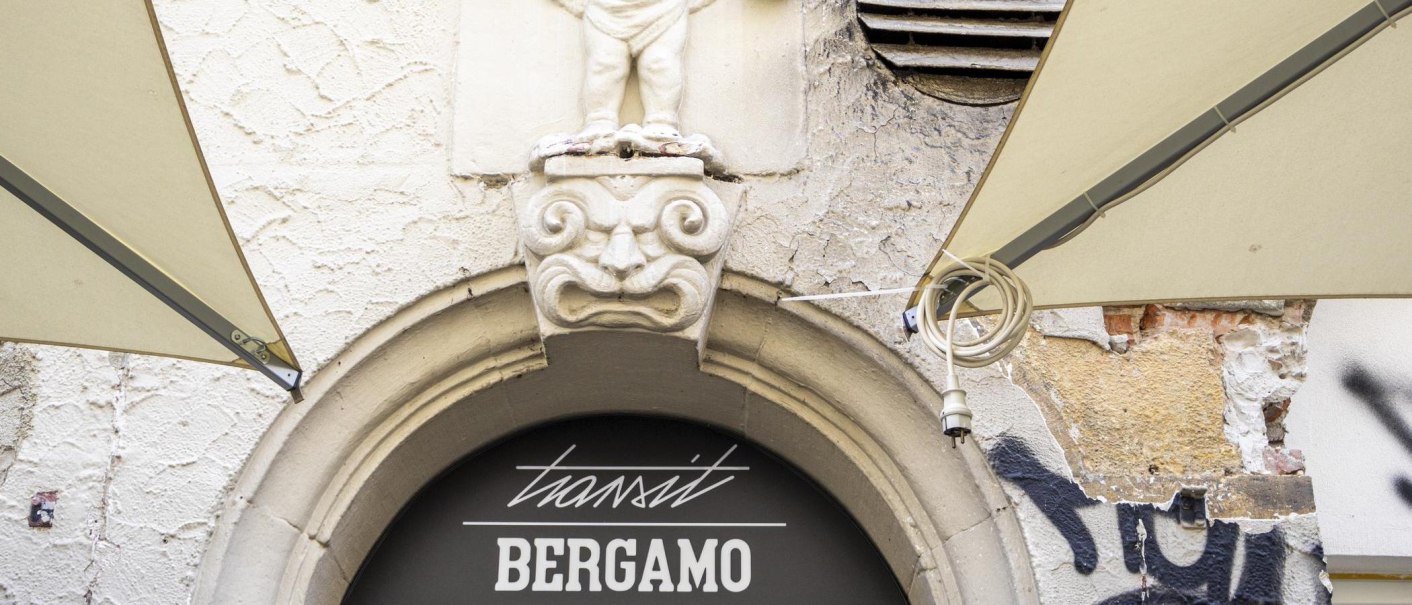Steinfigur über einem Torbogen mit der Aufschrift 'transit BERGAMO'. Graffiti und verwitterte Wand im Hintergrund., © SMG, Sarah Schmid