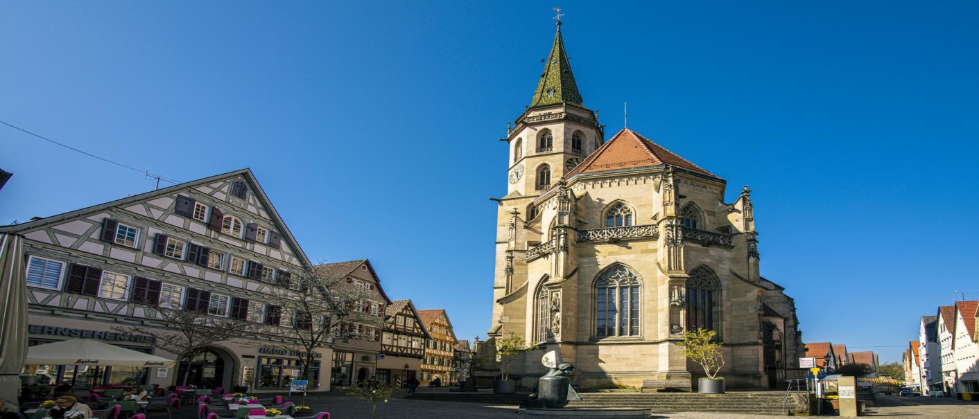 Die Schorndorfer Stadtkirche im Sonnenlicht, umgeben von Fachwerkhäusern und einem klaren blauen Himmel., © SMG, Sarah Schmid Die Schorndorfer Stadtkirche im Sonnenlicht, umgeben von Fachwerkhäusern und einem klaren blauen Himmel., © SMG, Sarah Schmid
