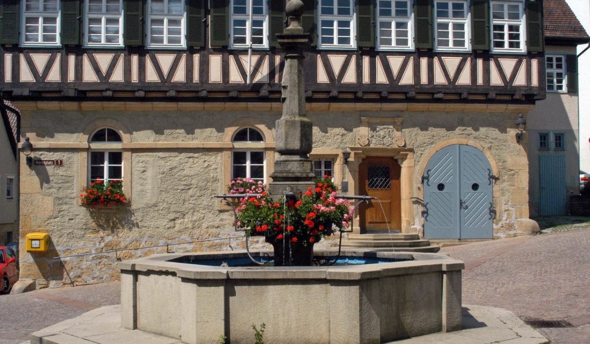 Fachwerkhaus mit Brunnen und Blumen im Vordergrund, gelber Briefkasten an der Wand, Tür mit Verzierungen, Fensterläden geöffnet., © Natur.Nah. Schönbuch & Heckengäu Fachwerkhaus mit Brunnen und Blumen im Vordergrund, gelber Briefkasten an der Wand, Tür mit Verzierungen, Fensterläden geöffnet., © Natur.Nah. Schönbuch & Heckengäu