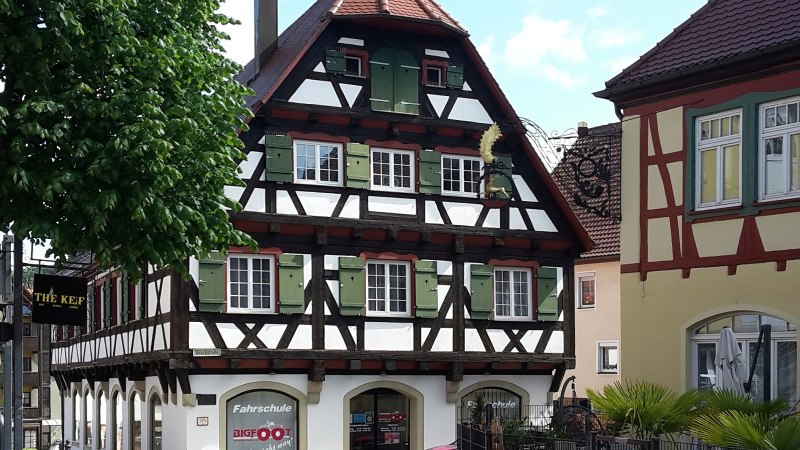 Alter Speicher - Fachwerkhaus mit dunklem Holz, weißen Gefachen und grünen Fensterläden in der Bildmitte, rechts daneben ein gelbes Haus mit rot-braunem Fachwerk im Obergeschoß und altem Wirtshausschild, © Petra Natzkowski