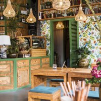 Gemütlicher Gastraum mit Holzmöbeln, bunten Blumen, Regalen voller Flaschen und Büchern. Helle Lampen und florale Tapete schaffen eine einladende Atmosphäre., © Vietal Kitchen Gemütlicher Gastraum mit Holzmöbeln, bunten Blumen, Regalen voller Flaschen und Büchern. Helle Lampen und florale Tapete schaffen eine einladende Atmosphäre., © Vietal Kitchen