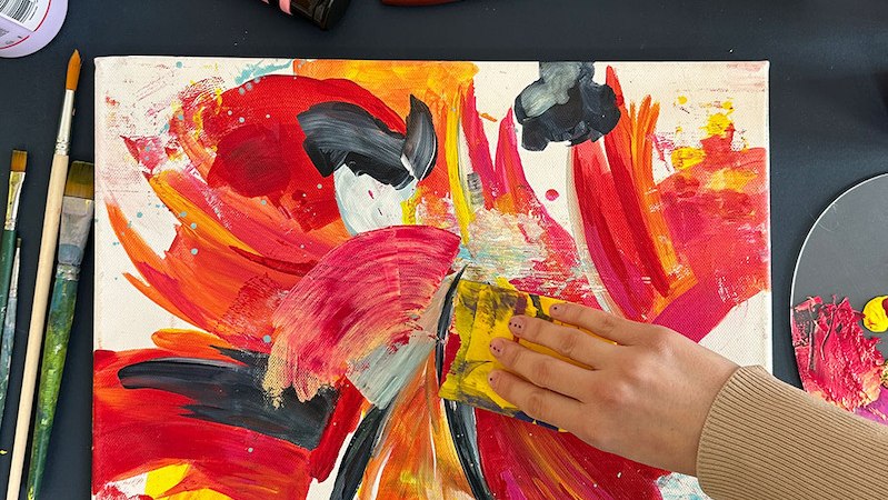 Hand malt mit Schwamm auf abstrakter Leinwand in Rot, Gelb und Schwarz. Pinsel und Farben liegen verstreut auf einem Tisch., © Mercedes-Benz AG Hand malt mit Schwamm auf abstrakter Leinwand in Rot, Gelb und Schwarz. Pinsel und Farben liegen verstreut auf einem Tisch., © Mercedes-Benz AG