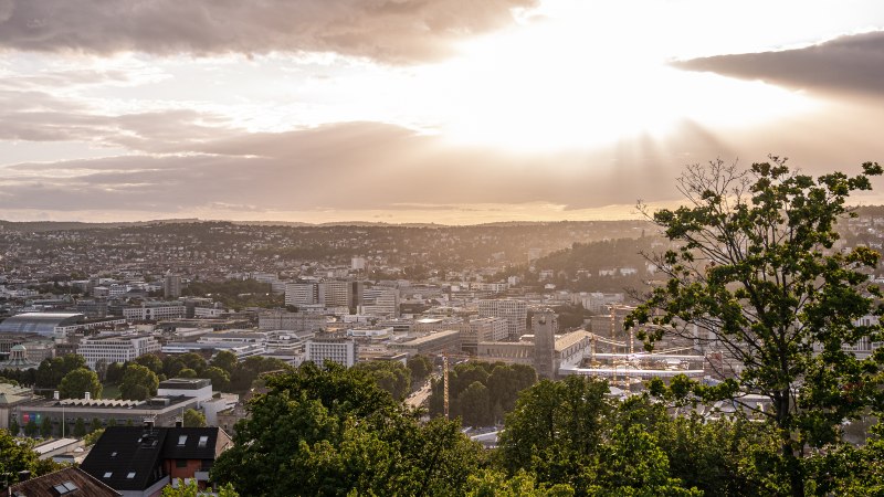Blick von der Uhlandshöhe auf Stuttgart bei Sonnenuntergang. Die Stadt liegt unter einem dramatischen Himmel mit Sonnenstrahlen und Wolken., © Christine Garcia, Urban Trickytine Blick von der Uhlandshöhe auf Stuttgart bei Sonnenuntergang. Die Stadt liegt unter einem dramatischen Himmel mit Sonnenstrahlen und Wolken., © Christine Garcia, Urban Trickytine