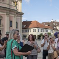 Gruppe applaudiert einer Frau vor einem historischen Gebäude in Ludwigsburg. Sonniger Tag, fröhliche Stimmung., © Tourismus & Events Ludwigsburg, Yakup Zeyrek