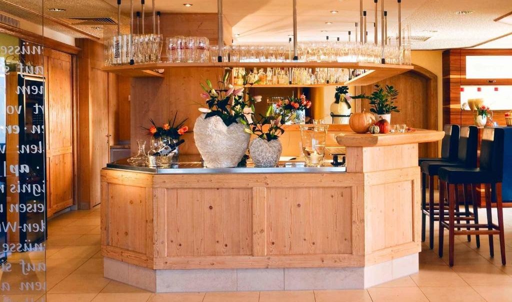 Gemütliche Holzbar mit Blumenvasen und Gläsern, umgeben von Barhockern. Die Einrichtung wirkt einladend und warm., © Nödinger Gastro GmbH