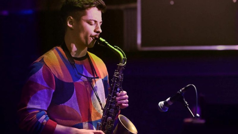 Ein Saxophonspieler in buntem Pullover spielt konzentriert auf einer B&uuml;hne. Ein Mikrofon ist vor ihm positioniert., &copy; Foto Gerhard Richter