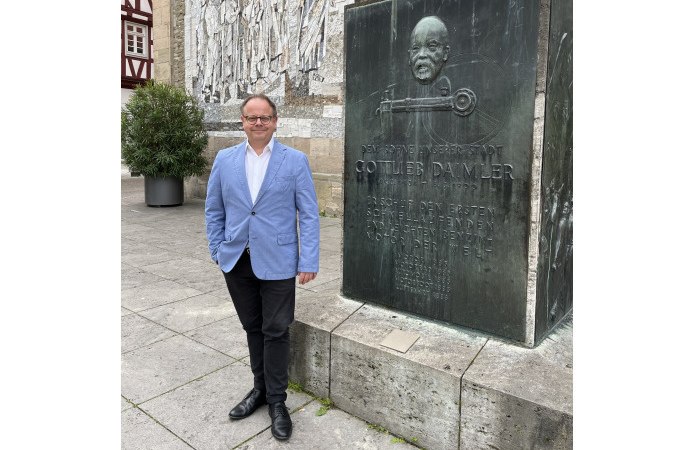 Ein Mann in einem blauen Sakko steht neben einem Denkmal von Gottlieb Daimler in Schorndorf. Im Hintergrund ist ein Wandrelief zu sehen., &copy; Eigenbetrieb Tourismus und Citymanagement Schorndorf