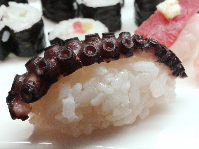 Nahaufnahme von Sushi mit Oktopus auf Reis, im Hintergrund weitere Sushirollen. Detailreiche Darstellung der Zutaten., &copy; Kultweine-Kochwelten-Kunst&uuml;cke - Kochschule Sonja Lenz