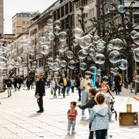 Ein Stra&szlig;enk&uuml;nstler erzeugt Seifenblasen auf einer belebten Stra&szlig;e. Kinder spielen begeistert mit den Blasen, w&auml;hrend Passanten zuschauen., &copy; Stuttgart-Marketing GmbH, Sarah Schmid