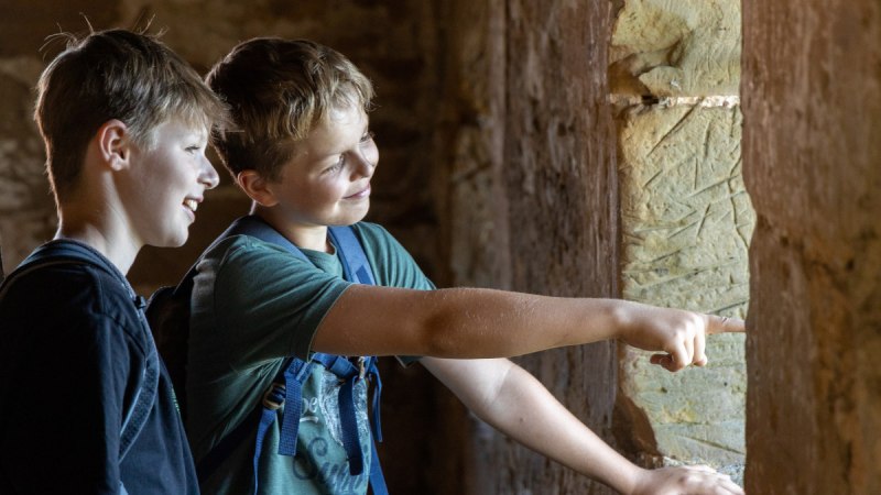 Zwei Jungen stehen in einer Burgruine und schauen lächelnd aus einem Fenster. Einer zeigt nach draußen., © Foto Thomas Zehnder Zwei Jungen stehen in einer Burgruine und schauen lächelnd aus einem Fenster. Einer zeigt nach draußen., © Foto Thomas Zehnder