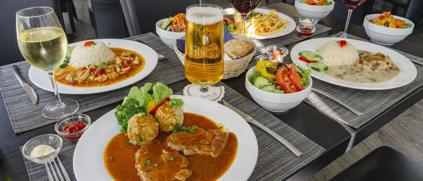 Ein Tisch mit verschiedenen Gerichten: Fleisch mit Soße, Reisgerichte, Salate. Getränke wie Bier und Wein sind ebenfalls zu sehen., © Plaza INN Stuttgart-Filderstadt Ein Tisch mit verschiedenen Gerichten: Fleisch mit Soße, Reisgerichte, Salate. Getränke wie Bier und Wein sind ebenfalls zu sehen., © Plaza INN Stuttgart-Filderstadt